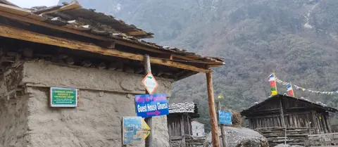 Hand-painted guest house and trekking-shop signs on a stone lodge wall in Ghunsa