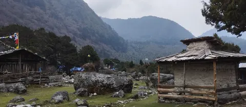 Timber Sherpa houses and boulders on the grassy floor of Ghunsa village, prayer flags behind