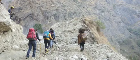 Trail cut into the cliffside above the Budhi Gandaki, with porters carrying doko baskets
