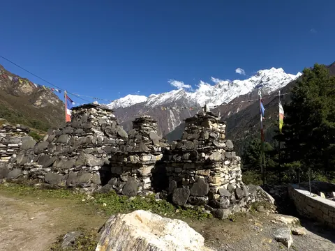 Old stone chortens and prayer flags below a snow-covered range