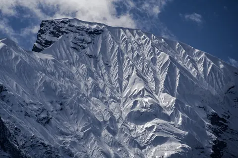 A steep, fluted snow face under a clearing sky