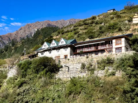 A stone lodge with green roofs on a terraced hillside below rocky peaks