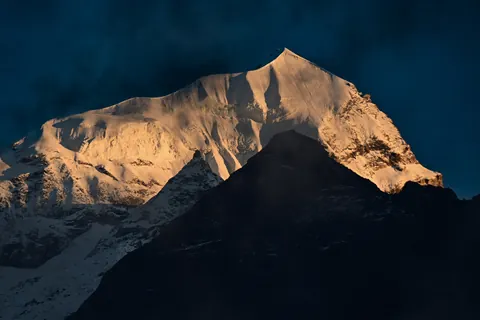 Late light turning a snow peak orange above a dark ridge
