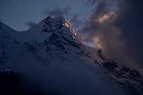 Evening cloud catching light around a dark snow peak
