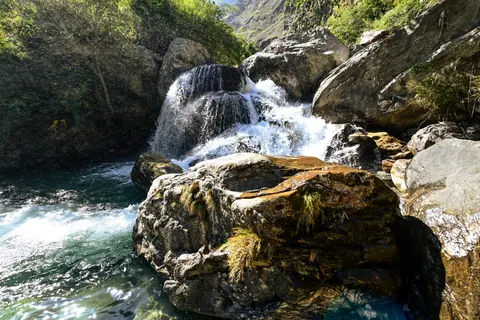 White water pouring around a mossy boulder into a green pool