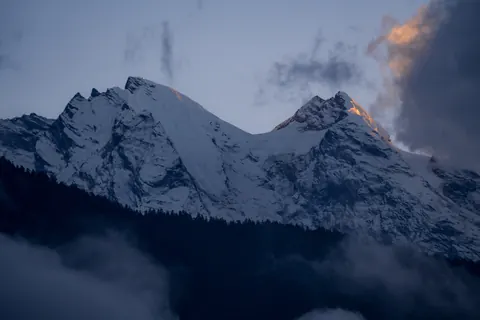 Two snow peaks with a touch of evening light above a cloud-filled valley