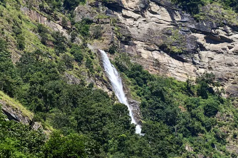 A long waterfall dropping down a rock cliff through green forest
