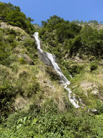 A waterfall cascading down a grassy, forested hillside under a blue sky
